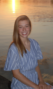 A woman in a striped dress smiles in front of a sunset. 